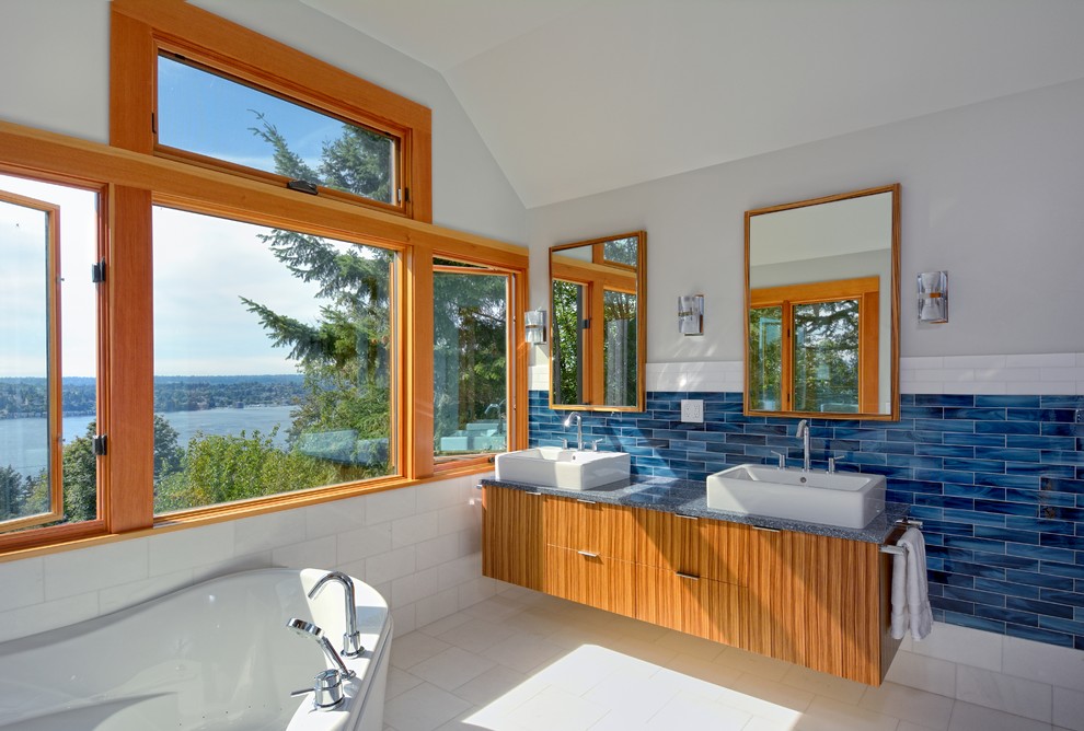 Идея дизайна: ванная комната в современном стиле с настольной раковиной, угловой ванной, плоскими фасадами, фасадами цвета дерева среднего тона, столешницей из искусственного кварца, синей плиткой и стеклянной плиткой