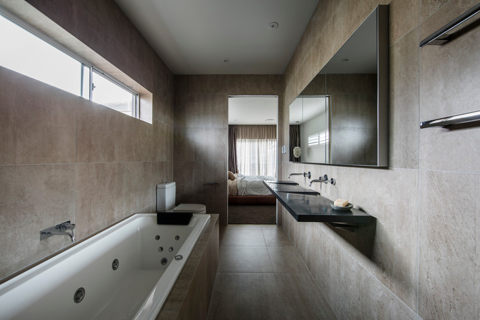 Modern inredning av ett mellanstort badrum, med ett undermonterat badkar, en toalettstol med separat cisternkåpa, beige kakel, stenhäll, beige väggar, cementgolv, ett integrerad handfat och bänkskiva i onyx