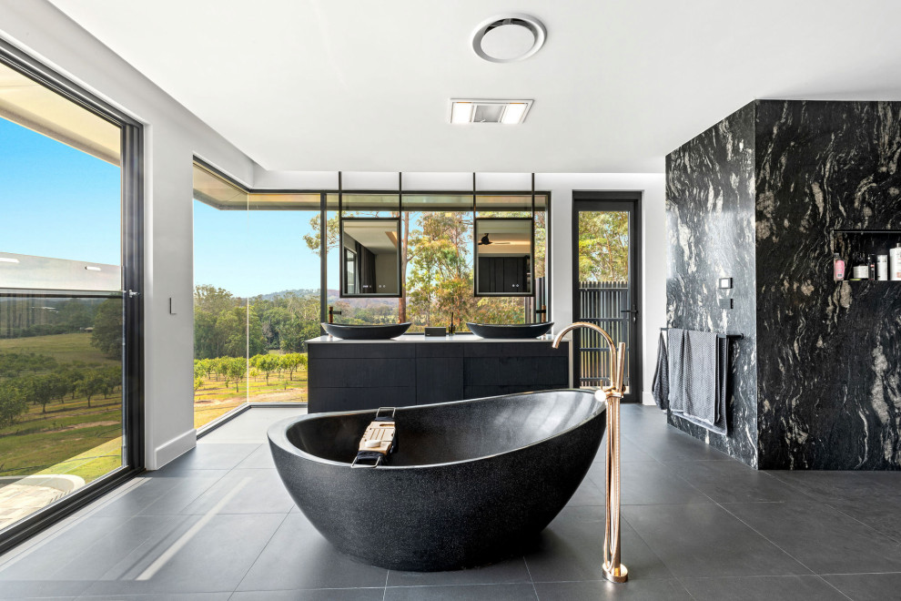 Photo of a large contemporary ensuite bathroom in Sunshine Coast with flat-panel cabinets, black cabinets, a freestanding bath, black and white tiles, stone slabs, white walls, a vessel sink, grey floors, double sinks, a walk-in shower, all types of toilet, porcelain flooring, solid surface worktops, an open shower, grey worktops, all types of ceiling and all types of wall treatment.