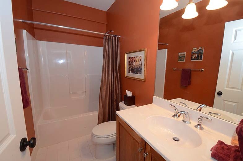 На фото: ванная комната среднего размера в классическом стиле с фасадами в стиле шейкер, фасадами цвета дерева среднего тона, ванной в нише, душем над ванной, раздельным унитазом, оранжевыми стенами, душевой кабиной, монолитной раковиной и столешницей из искусственного кварца