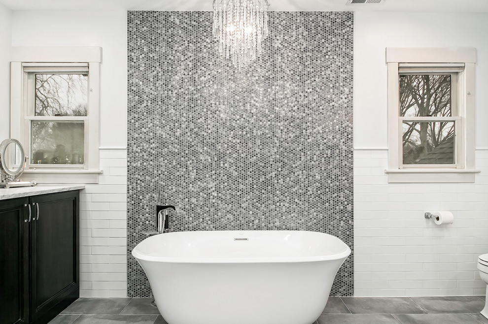Cette photo montre une salle de bain tendance de taille moyenne avec un placard avec porte à panneau encastré, des portes de placard noires, une baignoire indépendante, un carrelage blanc, un carrelage métro, un mur gris, un sol en carrelage de porcelaine et un sol gris.