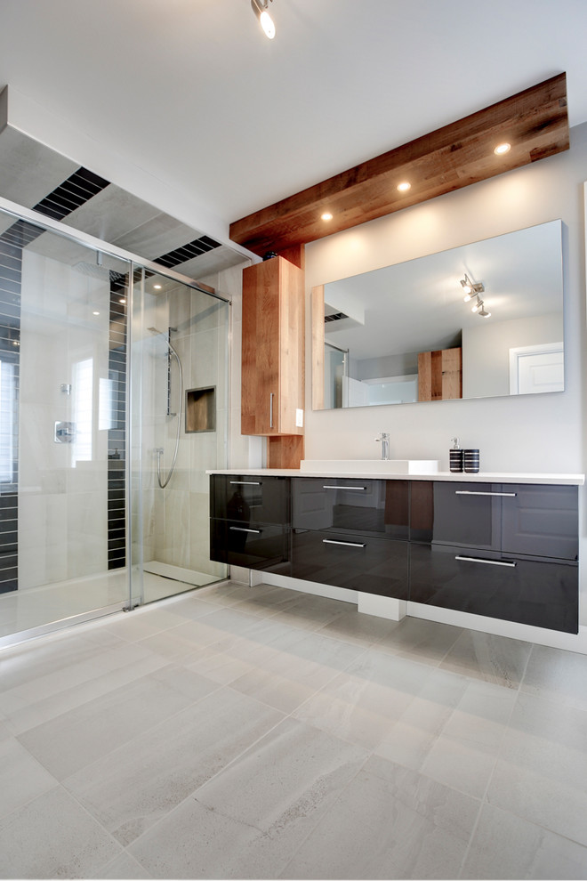 Large modern ensuite bathroom in Montreal with flat-panel cabinets, grey cabinets, a freestanding bath, a corner shower, a one-piece toilet, grey tiles, ceramic tiles, grey walls, ceramic flooring, a wall-mounted sink and laminate worktops.