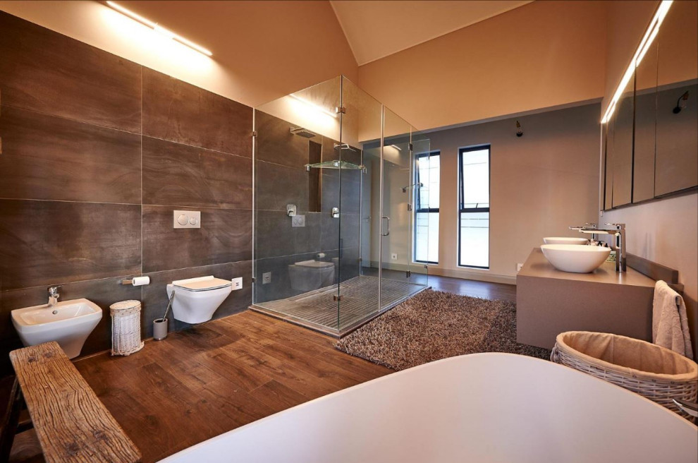 Foto på ett litet funkis grå en-suite badrum, med släta luckor, skåp i mörkt trä, ett fristående badkar, en hörndusch, en vägghängd toalettstol, grå kakel, mosaik, bänkskiva i kvarts, brunt golv och dusch med gångjärnsdörr