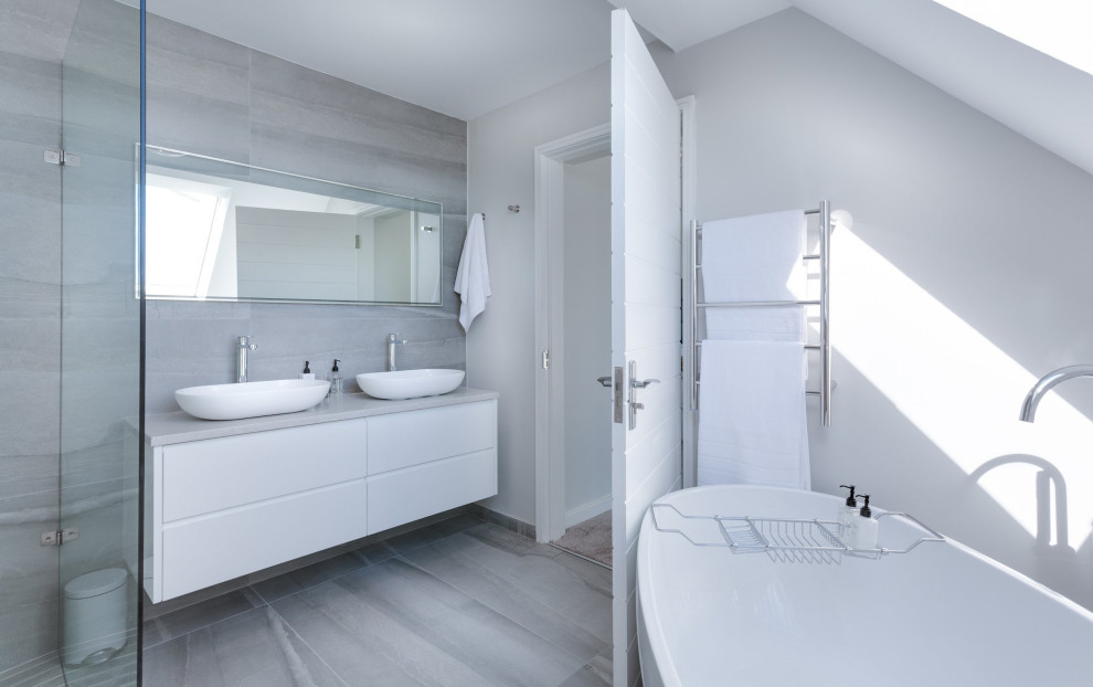 Réalisation d'une grande salle de bain principale design avec un placard à porte plane, des portes de placard blanches, une baignoire indépendante, une douche d'angle, un carrelage gris, un mur gris, une vasque, un sol gris et un plan de toilette gris.