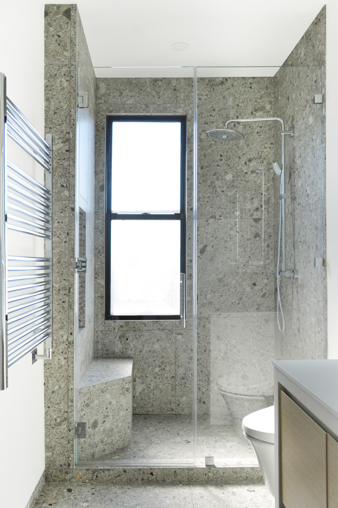Photo of a medium sized contemporary ensuite bathroom in New York with flat-panel cabinets, white cabinets, an alcove shower, a wall mounted toilet, white walls, terrazzo flooring, a submerged sink, solid surface worktops, grey floors, a hinged door, white worktops, a shower bench, double sinks and a built in vanity unit.