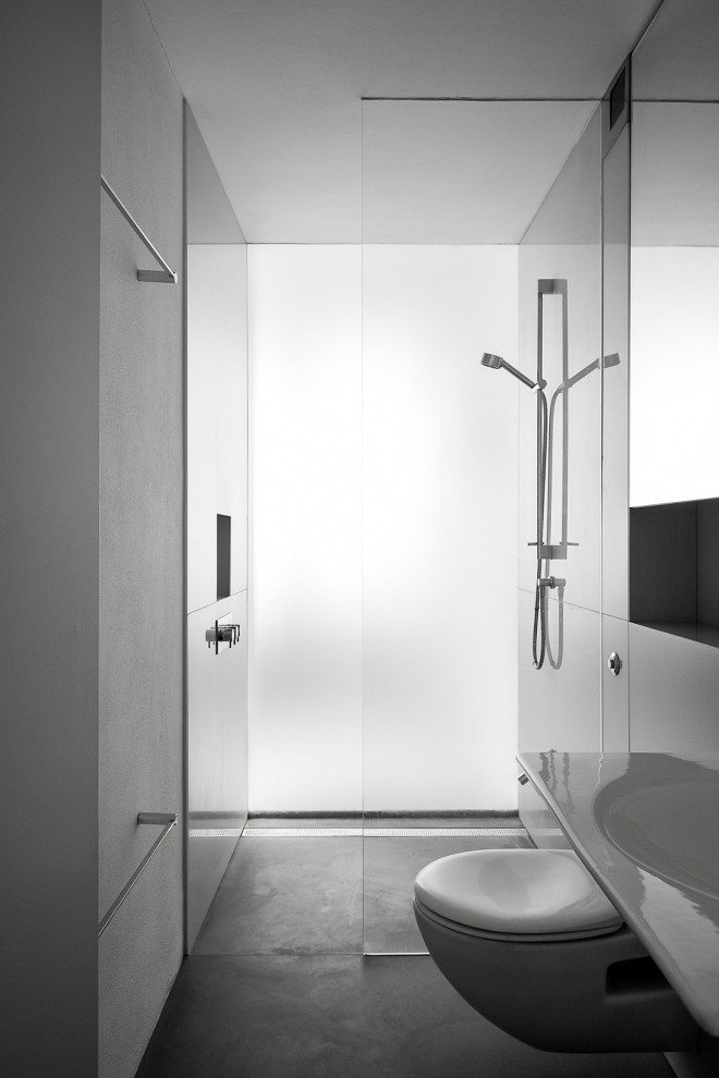 Modern inredning av ett mellanstort badrum med dusch, med en öppen dusch, en vägghängd toalettstol, grå väggar, betonggolv, ett väggmonterat handfat och grått golv