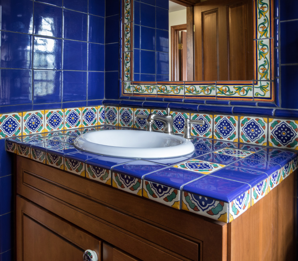 Amerikansk inredning av ett mellanstort badrum med dusch, med skåp i shakerstil, skåp i mellenmörkt trä, blå kakel, keramikplattor, ett nedsänkt handfat och kaklad bänkskiva