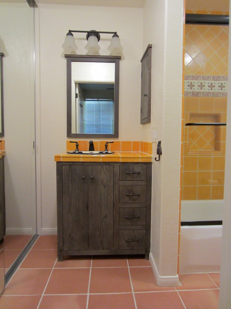 Idéer för att renovera ett litet rustikt en-suite badrum, med ett nedsänkt handfat, släta luckor, skåp i slitet trä, kaklad bänkskiva, ett badkar i en alkov, en dusch/badkar-kombination, en toalettstol med separat cisternkåpa, gul kakel, keramikplattor, beige väggar och klinkergolv i terrakotta