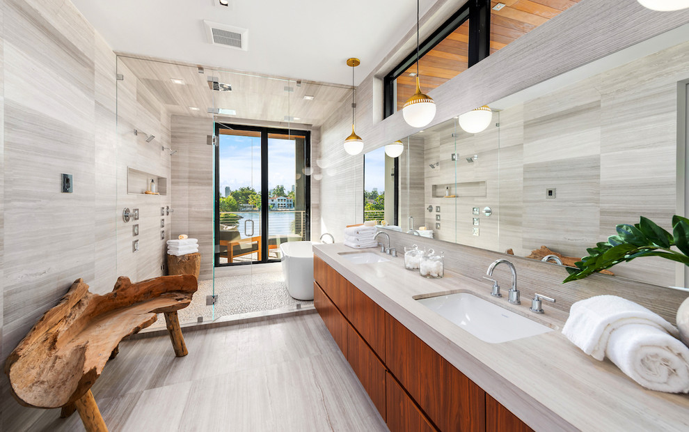 Cette image montre une salle de bain minimaliste en bois brun avec un placard à porte plane, une baignoire indépendante, un espace douche bain, un carrelage gris, un lavabo encastré, un sol beige, une cabine de douche à porte battante et un plan de toilette gris.