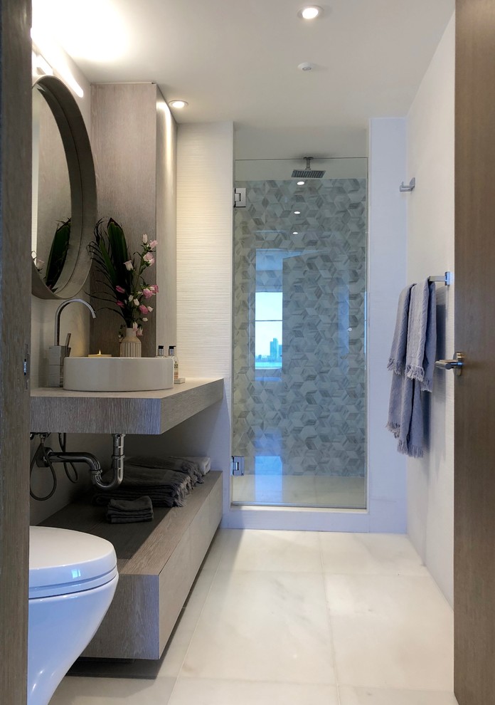 Photo of a medium sized modern shower room bathroom with flat-panel cabinets, distressed cabinets, an alcove shower, a wall mounted toilet, white tiles, ceramic tiles, white walls, marble flooring, a vessel sink, wooden worktops, white floors and a hinged door.