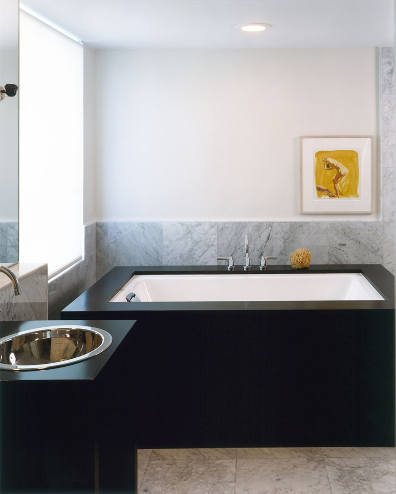 Contemporary bathroom in New York with a built-in sink, a submerged bath and grey tiles.