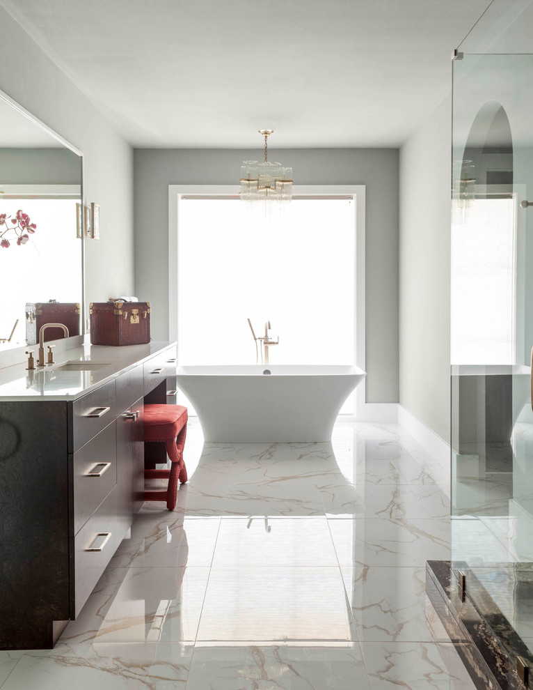 Cette photo montre une salle de bain principale tendance en bois foncé avec un placard à porte plane, un plan de toilette en verre recyclé, une baignoire indépendante, un mur beige, un sol en marbre, un lavabo encastré, un carrelage blanc et un carrelage de pierre.