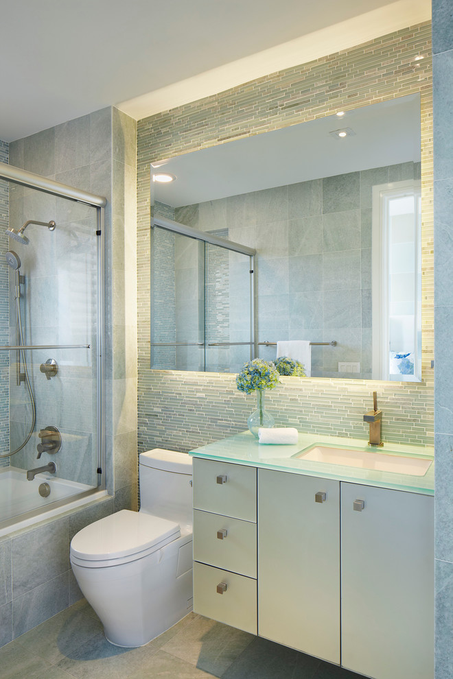 Modern inredning av ett mellanstort grön grönt badrum med dusch, med släta luckor, beige skåp, ett badkar i en alkov, en dusch/badkar-kombination, en toalettstol med hel cisternkåpa, grå kakel, marmorkakel, ett undermonterad handfat, bänkskiva i glas, grått golv och dusch med skjutdörr