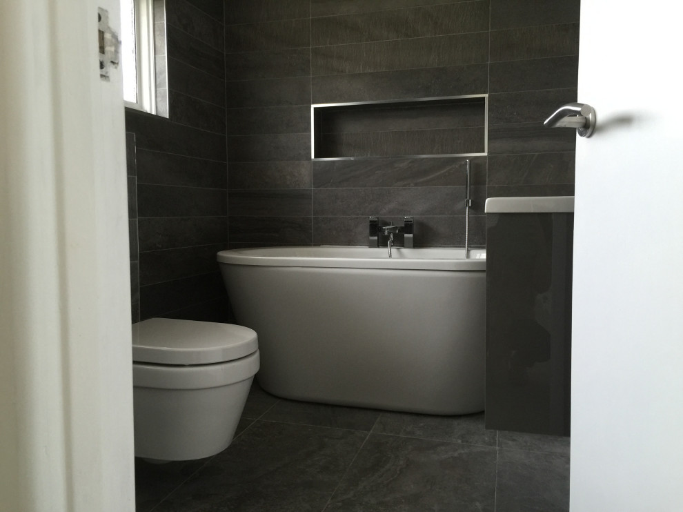 Exempel på ett mellanstort modernt badrum för barn, med släta luckor, grå skåp, ett fristående badkar, en hörndusch, en vägghängd toalettstol, grå kakel, keramikplattor, grå väggar, klinkergolv i keramik, ett väggmonterat handfat, grått golv och dusch med gångjärnsdörr