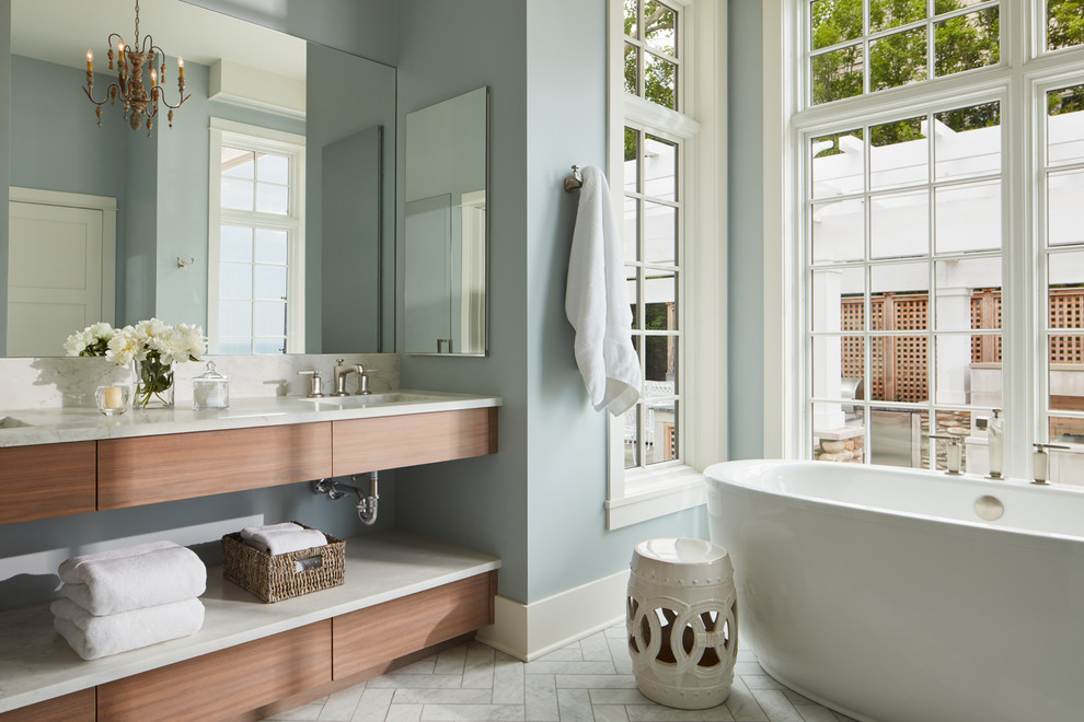 Maritim inredning av ett mellanstort en-suite badrum, med släta luckor, skåp i mellenmörkt trä, ett fristående badkar, blå väggar, marmorgolv, ett undermonterad handfat, marmorbänkskiva och vitt golv