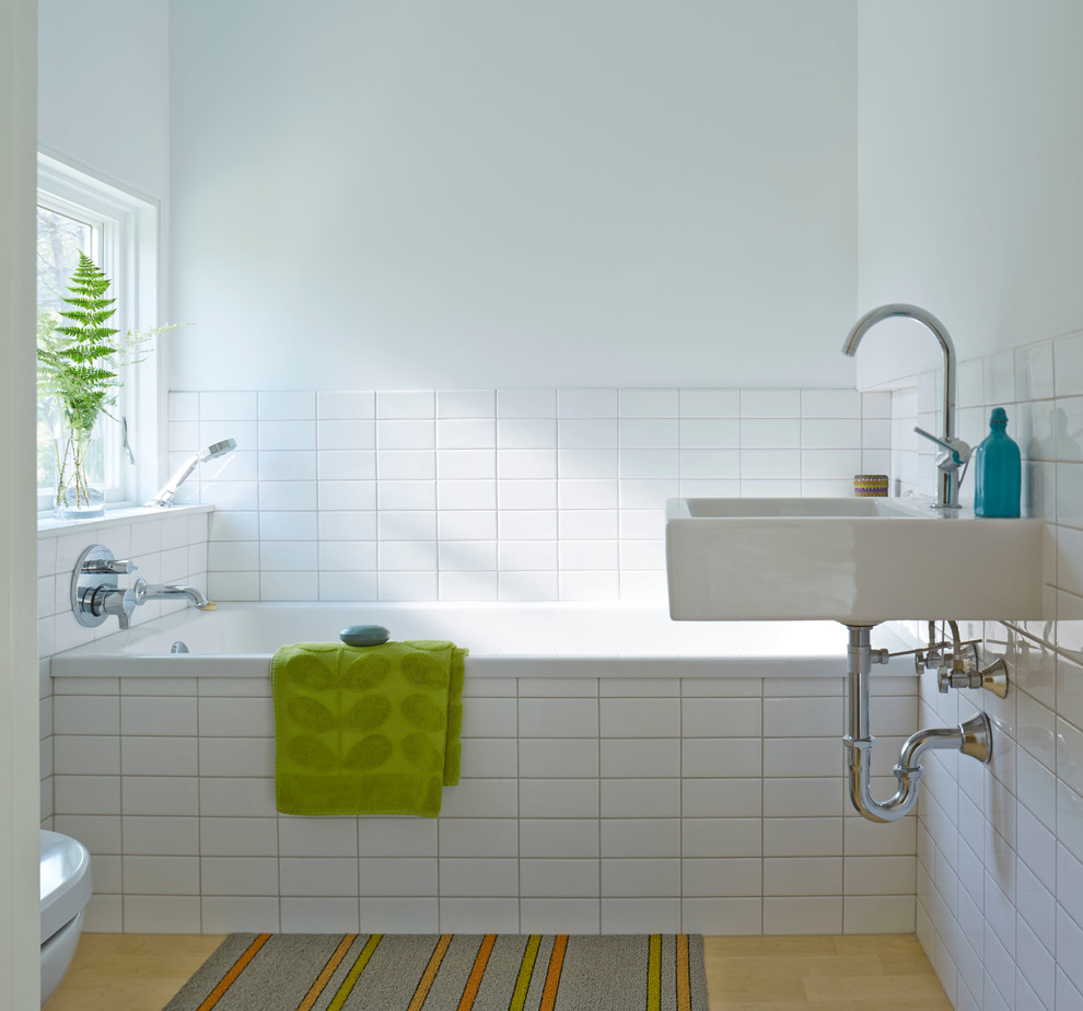 Ejemplo de cuarto de baño principal actual pequeño con bañera encastrada, sanitario de una pieza, baldosas y/o azulejos blancos, paredes blancas, lavabo suspendido y suelo de madera clara
