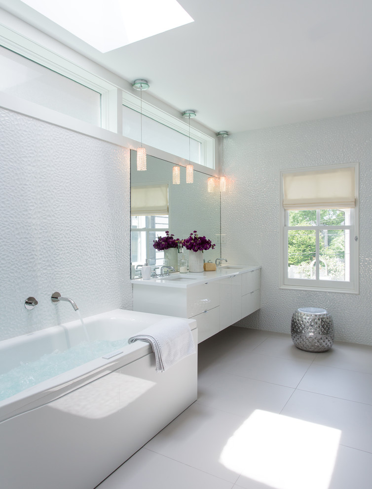 Modern inredning av ett stort vit vitt en-suite badrum, med ett undermonterad handfat, släta luckor, vita skåp, vita väggar, ett fristående badkar, klinkergolv i porslin och bänkskiva i akrylsten