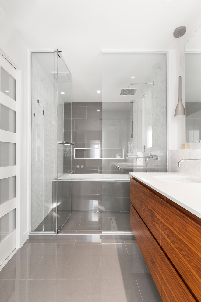Idéer för ett mellanstort 50 tals en-suite badrum, med släta luckor, skåp i mellenmörkt trä, ett platsbyggt badkar, en dusch/badkar-kombination, en toalettstol med hel cisternkåpa, vit kakel, marmorkakel, grå väggar, klinkergolv i porslin, ett undermonterad handfat, bänkskiva i kvarts, grått golv och dusch med gångjärnsdörr