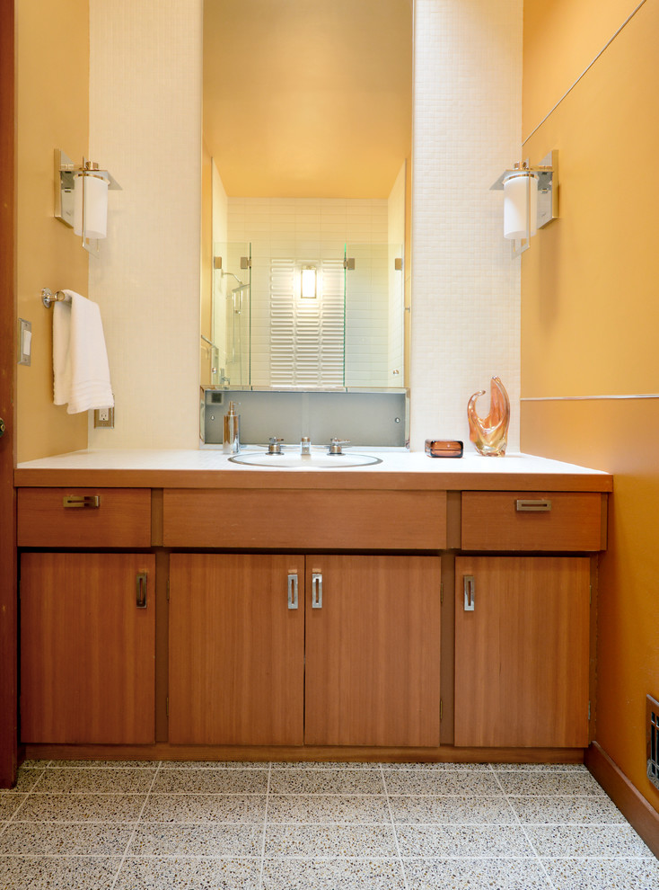 Immagine di una stanza da bagno design di medie dimensioni con pareti gialle, pavimento in laminato, doccia alcova, lavabo integrato, top piastrellato, ante lisce, ante in legno scuro e porta doccia a battente