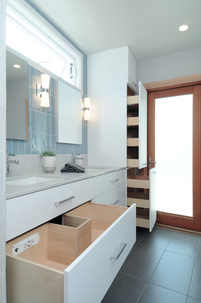 Inredning av ett retro stort badrum, med släta luckor, vita skåp, ett fristående badkar, en öppen dusch, en toalettstol med hel cisternkåpa, porslinskakel, grå väggar, ett undermonterad handfat och laminatbänkskiva