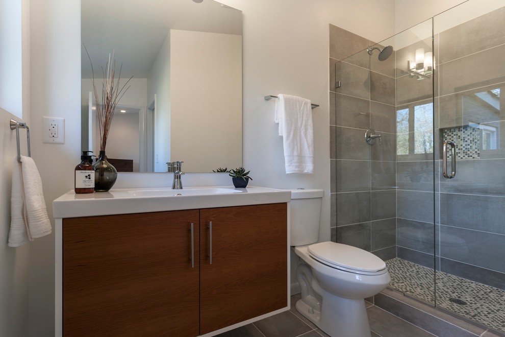 Photo of a medium sized midcentury ensuite bathroom in Other with a console sink, flat-panel cabinets, medium wood cabinets, solid surface worktops, a one-piece toilet, grey tiles, ceramic tiles, white walls and ceramic flooring.
