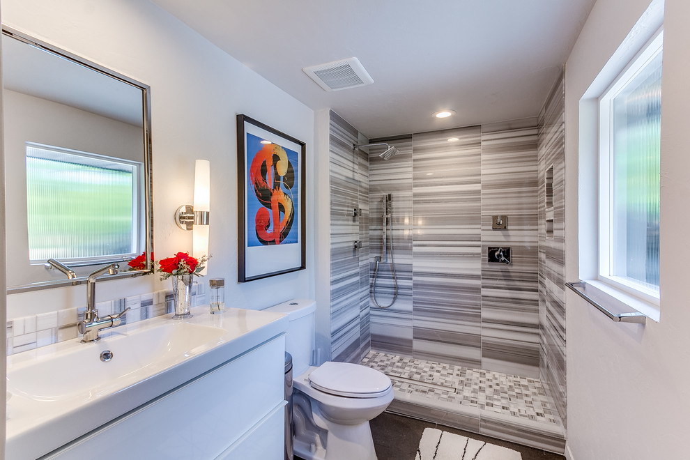 Example of a large mid-century modern 3/4 gray tile, white tile and ceramic tile brown floor bathroom design in Oklahoma City with flat-panel cabinets, white cabinets, a one-piece toilet, white walls and an integrated sink
