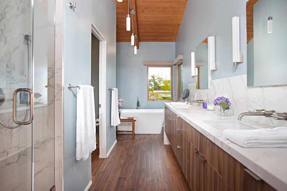 Bild på ett 50 tals en-suite badrum, med släta luckor, skåp i mörkt trä, ett fristående badkar, en dusch i en alkov, blå väggar, ett undermonterad handfat, brunt golv och dusch med gångjärnsdörr