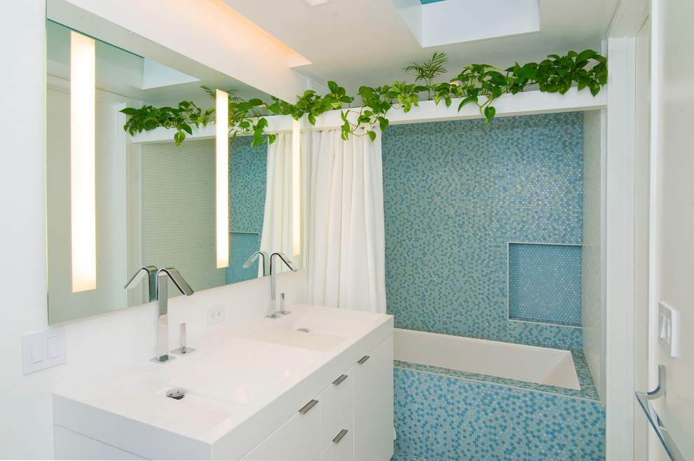Стильный дизайн: ванная комната среднего размера в современном стиле с плоскими фасадами, белыми фасадами, ванной в нише, душем над ванной, синей плиткой, плиткой мозаикой, белыми стенами, душевой кабиной, монолитной раковиной, столешницей из искусственного камня, шторкой для ванной и белой столешницей - последний тренд