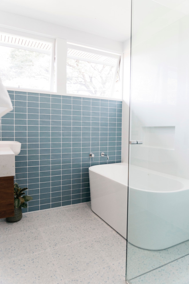 Bild på ett litet retro vit vitt badrum, med släta luckor, skåp i mellenmörkt trä, ett fristående badkar, en hörndusch, blå kakel, porslinskakel, vita väggar, terrazzogolv, ett nedsänkt handfat, bänkskiva i kvarts, grått golv och dusch med gångjärnsdörr