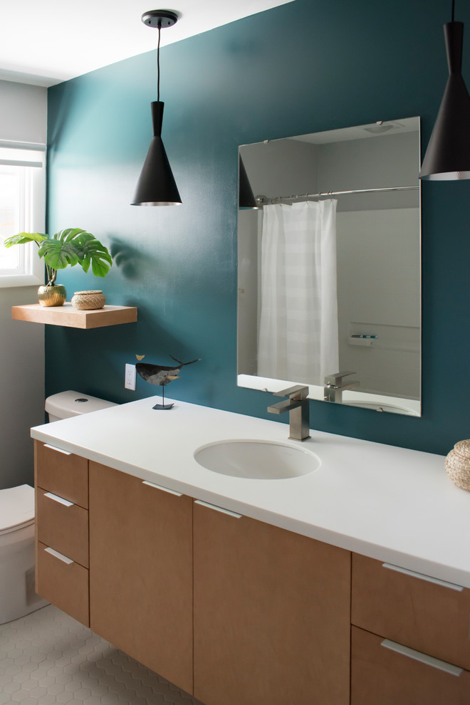 Cette photo montre une salle d'eau rétro en bois clair de taille moyenne avec un placard à porte plane, WC séparés, un mur bleu, un sol en carrelage de porcelaine, un lavabo encastré, un plan de toilette en surface solide, un sol blanc et un plan de toilette blanc.