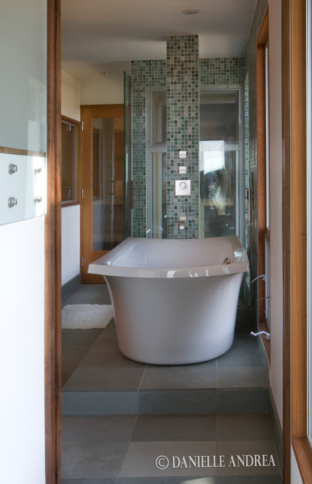 Design ideas for a large midcentury ensuite bathroom in Santa Barbara with flat-panel cabinets, medium wood cabinets, an alcove shower, grey tiles, a submerged sink, grey floors, a hinged door, white worktops, a freestanding bath, glass sheet walls and white walls.