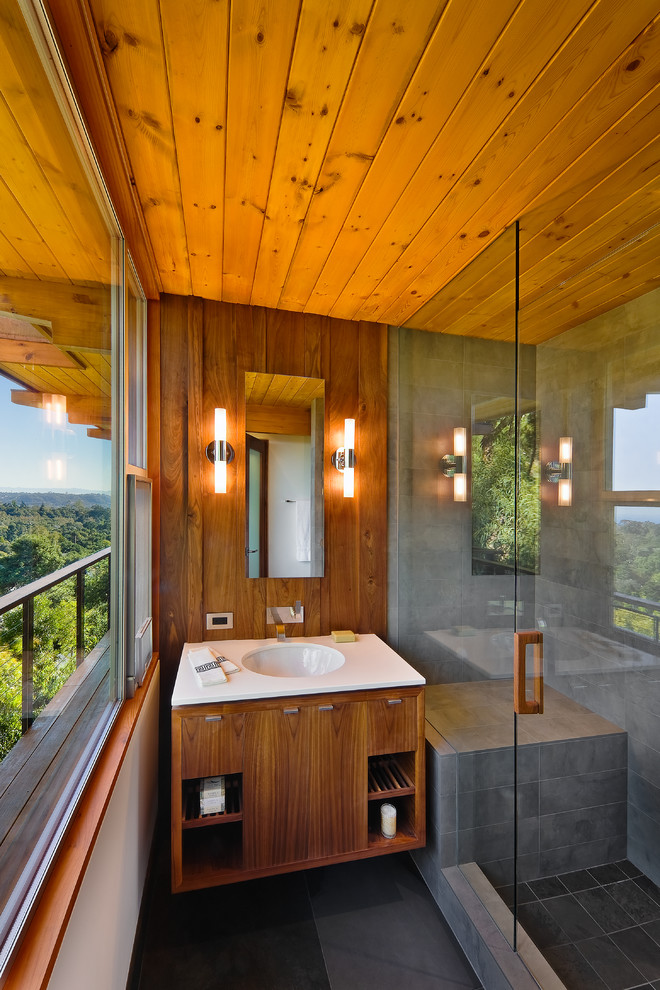 Cette image montre une salle de bain vintage en bois brun de taille moyenne avec un lavabo encastré, un placard à porte plane, un carrelage gris, un mur marron, un sol gris, une cabine de douche à porte battante et un plan de toilette blanc.
