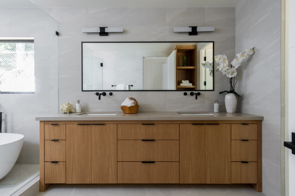 Aménagement d'une salle de bain principale rétro en bois clair avec un placard à porte plane, une baignoire indépendante, un carrelage gris, un mur gris, un lavabo encastré, un sol gris et un plan de toilette marron.