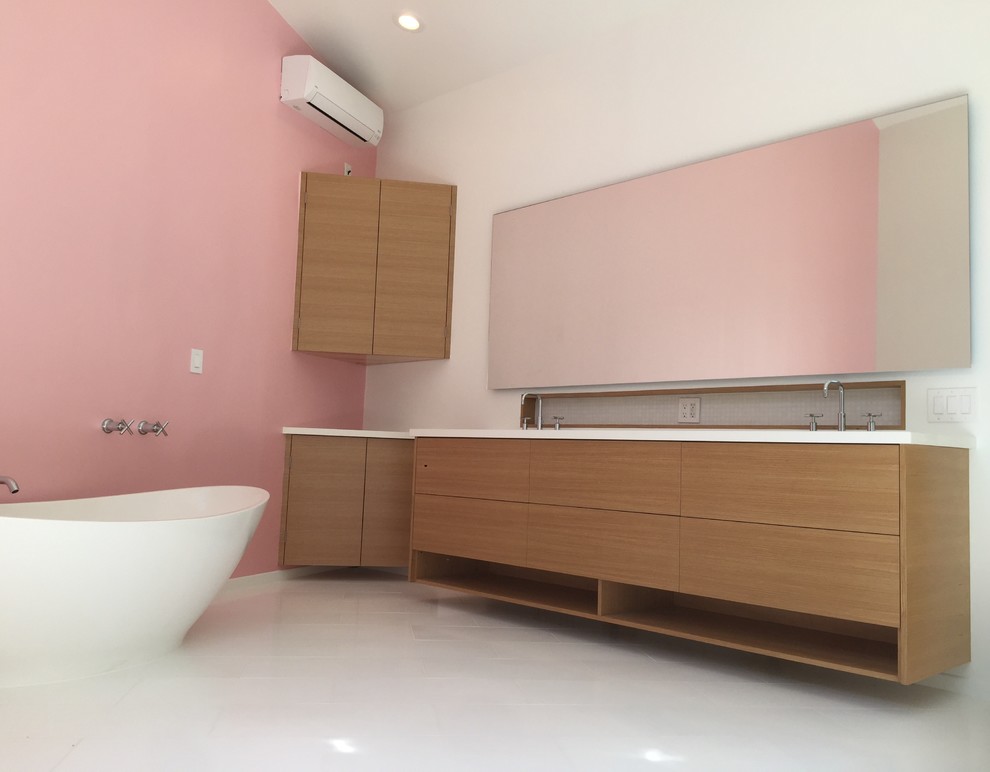 Inspiration for a medium sized modern ensuite bathroom in Los Angeles with flat-panel cabinets, medium wood cabinets, a freestanding bath, grey tiles, mosaic tiles, pink walls, porcelain flooring, solid surface worktops, white floors and white worktops.