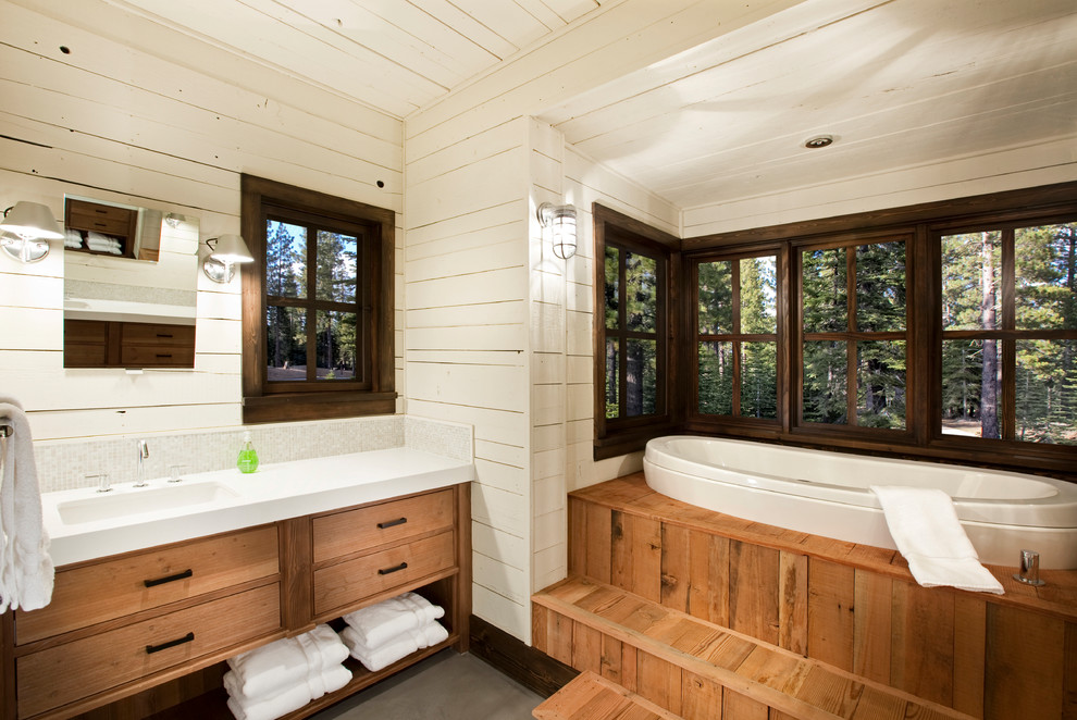 Réalisation d'une salle d'eau chalet en bois brun avec un placard à porte plane, une baignoire posée, un mur blanc, un lavabo encastré, un sol gris et sol en béton ciré.