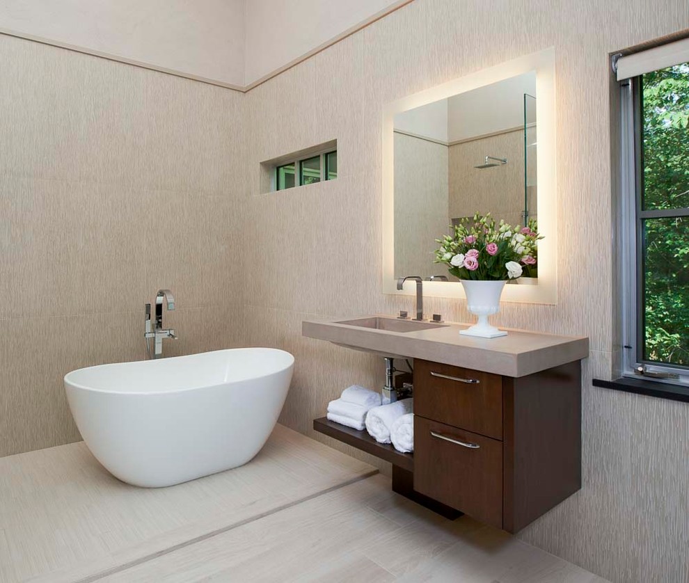 Photo of a medium sized retro ensuite bathroom in Detroit with flat-panel cabinets, brown cabinets, a freestanding bath, a shower/bath combination, a one-piece toilet, beige tiles, ceramic tiles, beige walls, ceramic flooring, an integrated sink, concrete worktops, beige floors, an open shower and beige worktops.