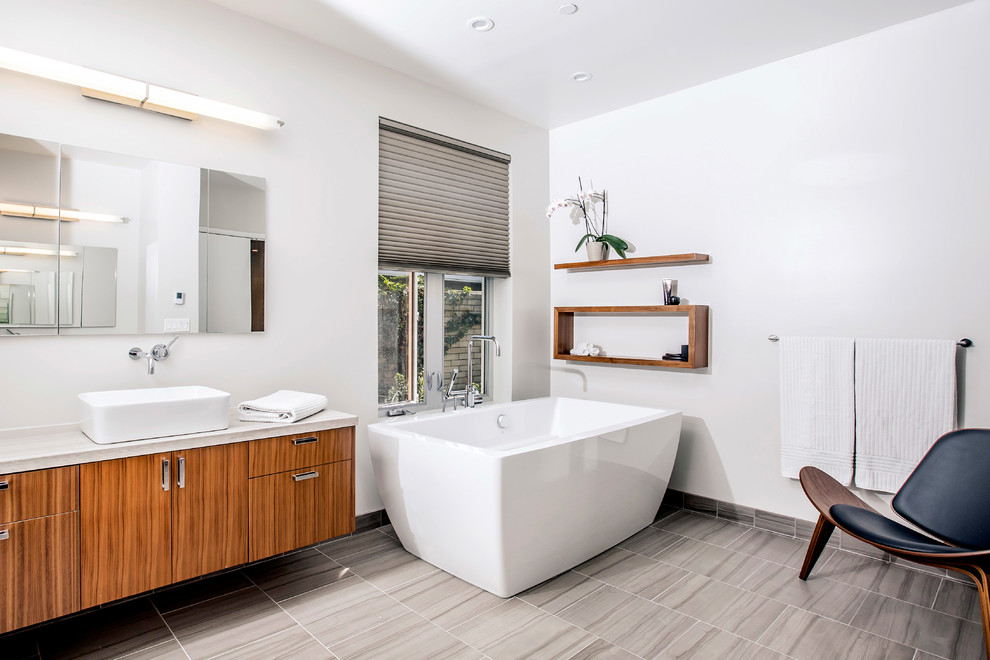 Cette photo montre une salle de bain tendance en bois brun avec un placard à porte plane, une baignoire indépendante, un mur blanc, une vasque, un sol gris et un plan de toilette beige.