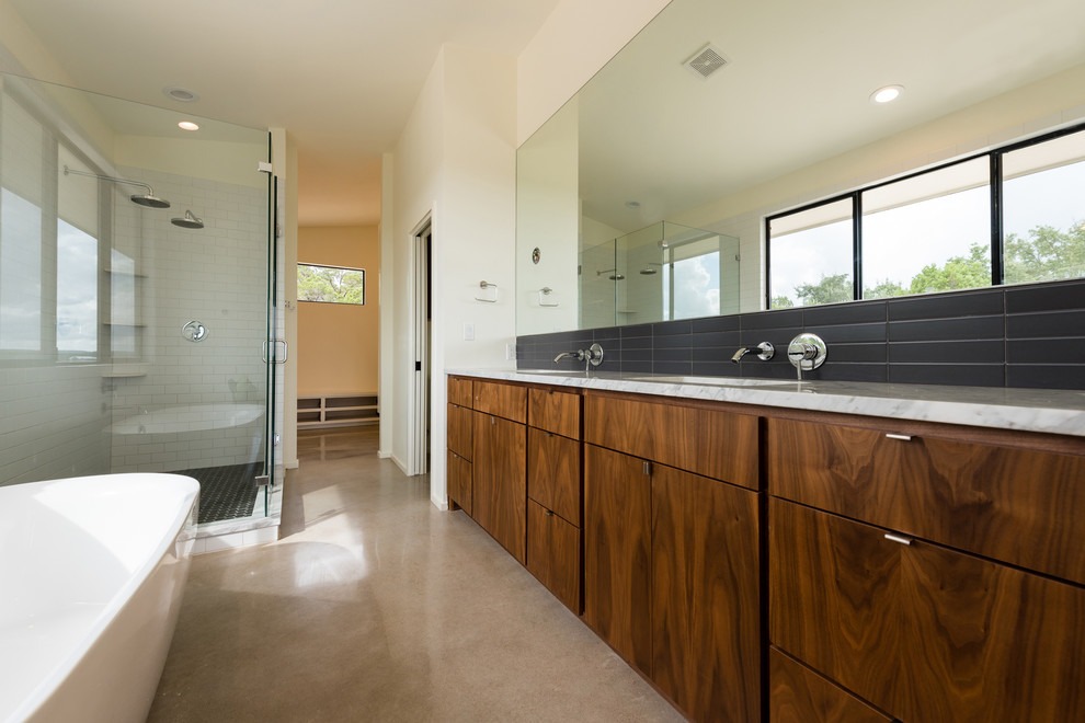 This is an example of a large retro ensuite bathroom in Austin with flat-panel cabinets, medium wood cabinets, a freestanding bath, a corner shower, a two-piece toilet, white tiles, metro tiles, white walls, concrete flooring, a submerged sink and marble worktops.