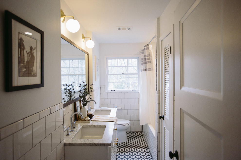 Klassisk inredning av ett mellanstort badrum med dusch, med släta luckor, vita skåp, ett badkar i en alkov, en dusch/badkar-kombination, en toalettstol med hel cisternkåpa, vit kakel, porslinskakel, vita väggar, klinkergolv i keramik, ett undermonterad handfat, marmorbänkskiva, flerfärgat golv och dusch med duschdraperi