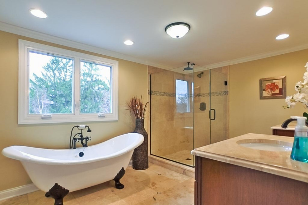 Idées déco pour une salle de bain principale rétro en bois brun avec un placard à porte shaker, une baignoire sur pieds, une douche d'angle, un carrelage beige, du carrelage en pierre calcaire, un mur beige, un sol en calcaire, un lavabo encastré, un plan de toilette en calcaire, un sol beige, une cabine de douche à porte battante, un plan de toilette multicolore, meuble double vasque et meuble-lavabo sur pied.