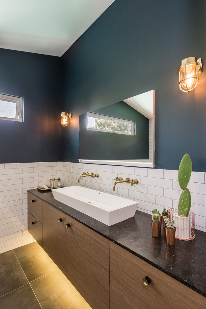Example of a mid-sized trendy 3/4 white tile and subway tile ceramic tile and brown floor bathroom design in Los Angeles with flat-panel cabinets, medium tone wood cabinets, a wall-mount toilet, blue walls, a vessel sink and soapstone countertops