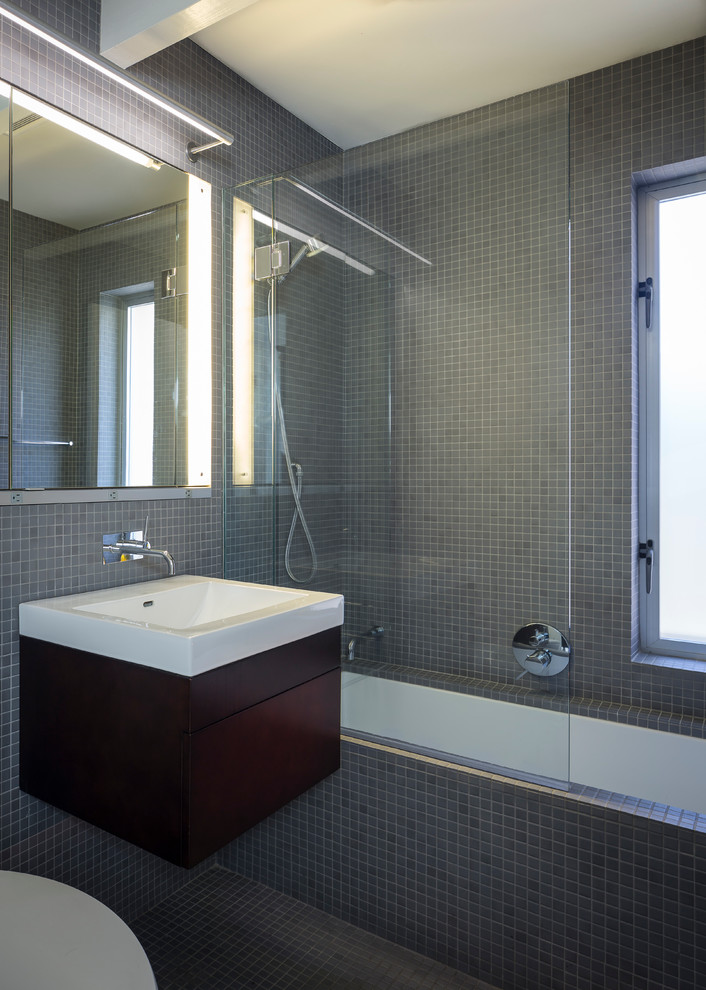 This is an example of a midcentury half tiled bathroom in San Francisco with an integrated sink, flat-panel cabinets, dark wood cabinets, a shower/bath combination, grey tiles and a submerged bath.