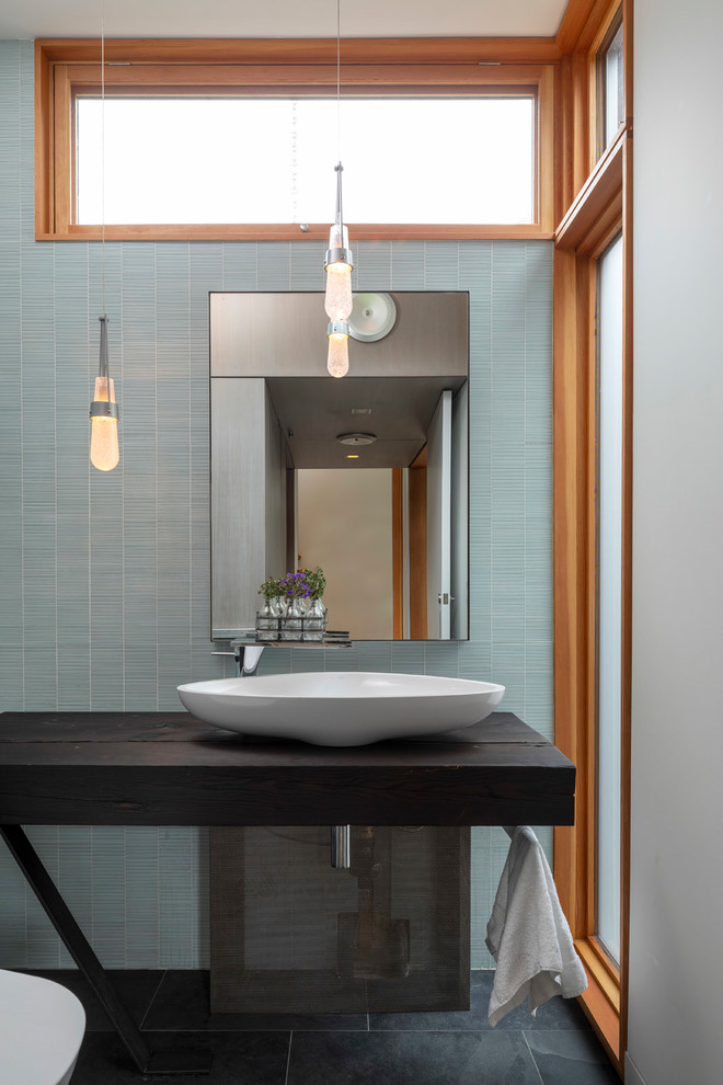 Ispirazione per una stanza da bagno moderna con piastrelle blu, piastrelle di vetro, pavimento in ardesia, lavabo a bacinella, top in legno, pavimento nero e top nero
