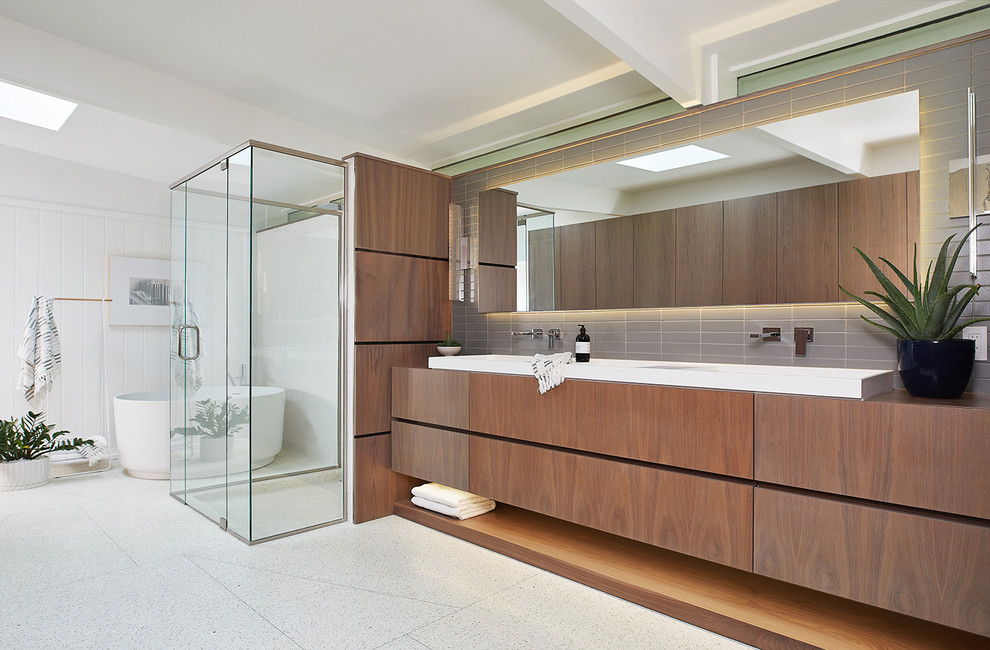 Inspiration for an expansive midcentury ensuite bathroom in Grand Rapids with flat-panel cabinets, a freestanding bath, a built-in shower, grey tiles, metro tiles, white walls, concrete flooring, a trough sink, white floors, a hinged door, dark wood cabinets and wooden worktops.