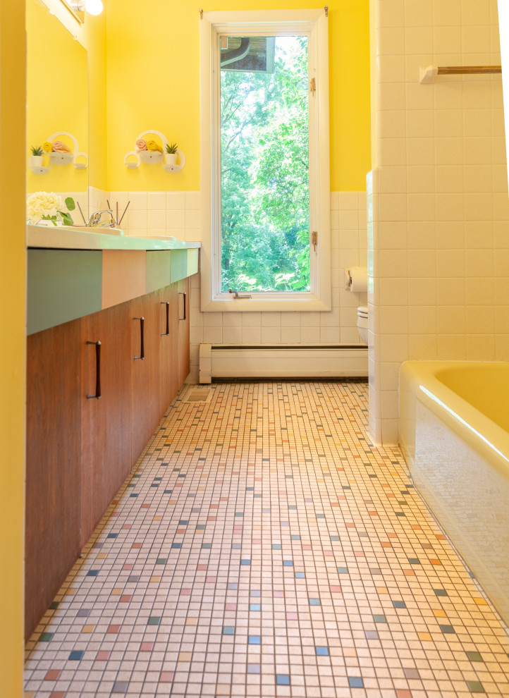 Photo of a small retro ensuite bathroom in Detroit with flat-panel cabinets, brown cabinets, an alcove bath, an alcove shower, a two-piece toilet, white tiles, ceramic tiles, yellow walls, ceramic flooring, a built-in sink, laminate worktops, multi-coloured floors, a shower curtain, white worktops, a single sink and a built in vanity unit.