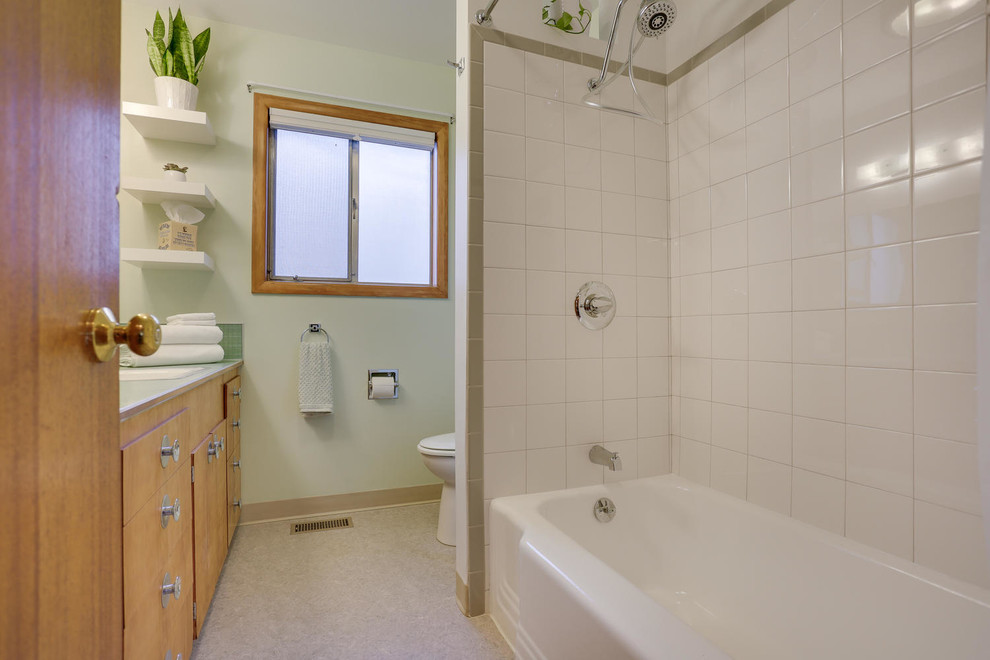 Пример оригинального дизайна: главная ванная комната среднего размера в стиле ретро с плоскими фасадами, фасадами цвета дерева среднего тона, ванной в нише, душем над ванной, раздельным унитазом, серой плиткой, керамической плиткой, зелеными стенами, полом из линолеума, накладной раковиной, столешницей из ламината, зеленым полом и шторкой для ванной