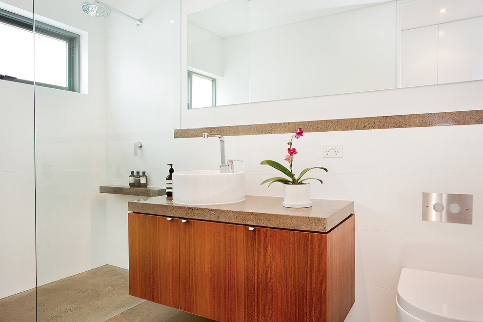 Bild på ett mellanstort funkis badrum med dusch, med släta luckor, skåp i mellenmörkt trä, en öppen dusch, en vägghängd toalettstol, vit kakel, porslinskakel, vita väggar, betonggolv, ett fristående handfat, brunt golv och med dusch som är öppen