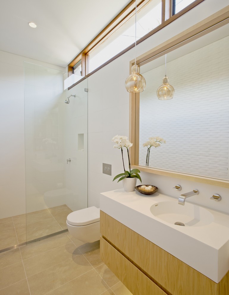 シドニーにある高級な広いコンテンポラリースタイルのおしゃれなバスルーム (浴槽なし) (一体型シンク、フラットパネル扉のキャビネット、淡色木目調キャビネット、人工大理石カウンター、オープン型シャワー、壁掛け式トイレ、白いタイル、セラミックタイル、白い壁、ライムストーンの床、オープンシャワー) の写真