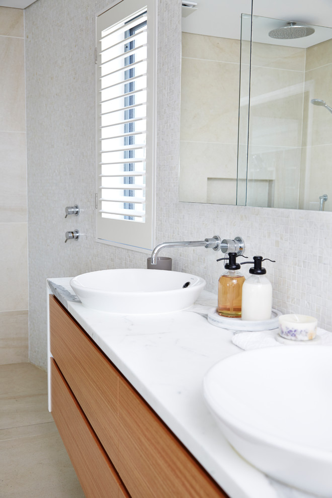 Пример оригинального дизайна: главная ванная комната в современном стиле с фасадами островного типа, светлыми деревянными фасадами, открытым душем, инсталляцией, бежевой плиткой, плиткой мозаикой, белыми стенами, полом из керамогранита, накладной раковиной и мраморной столешницей