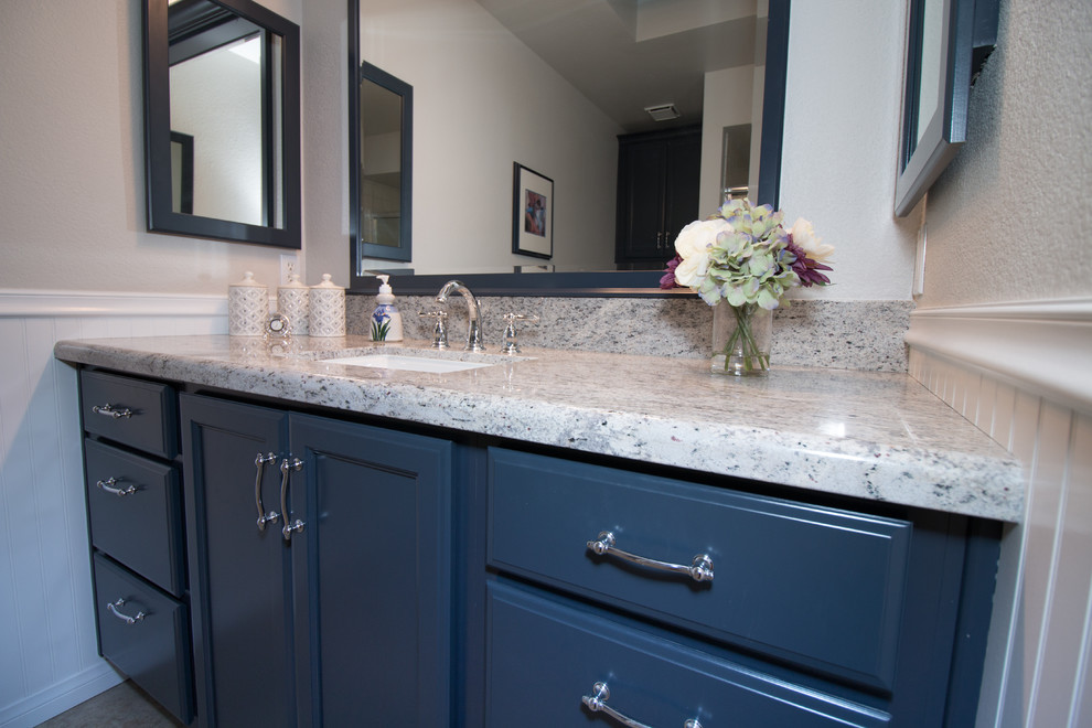 Foto de cuarto de baño tradicional de tamaño medio con lavabo bajoencimera, armarios con paneles lisos, puertas de armario azules, encimera de granito, baldosas y/o azulejos beige y paredes grises